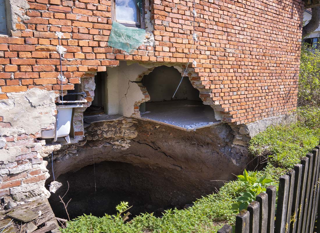 Sinkhole Insurance - A Large Sinkhole at the Foot of the House after an Earthquake Exposing Brick and Foundation Making It Uninhabitable
